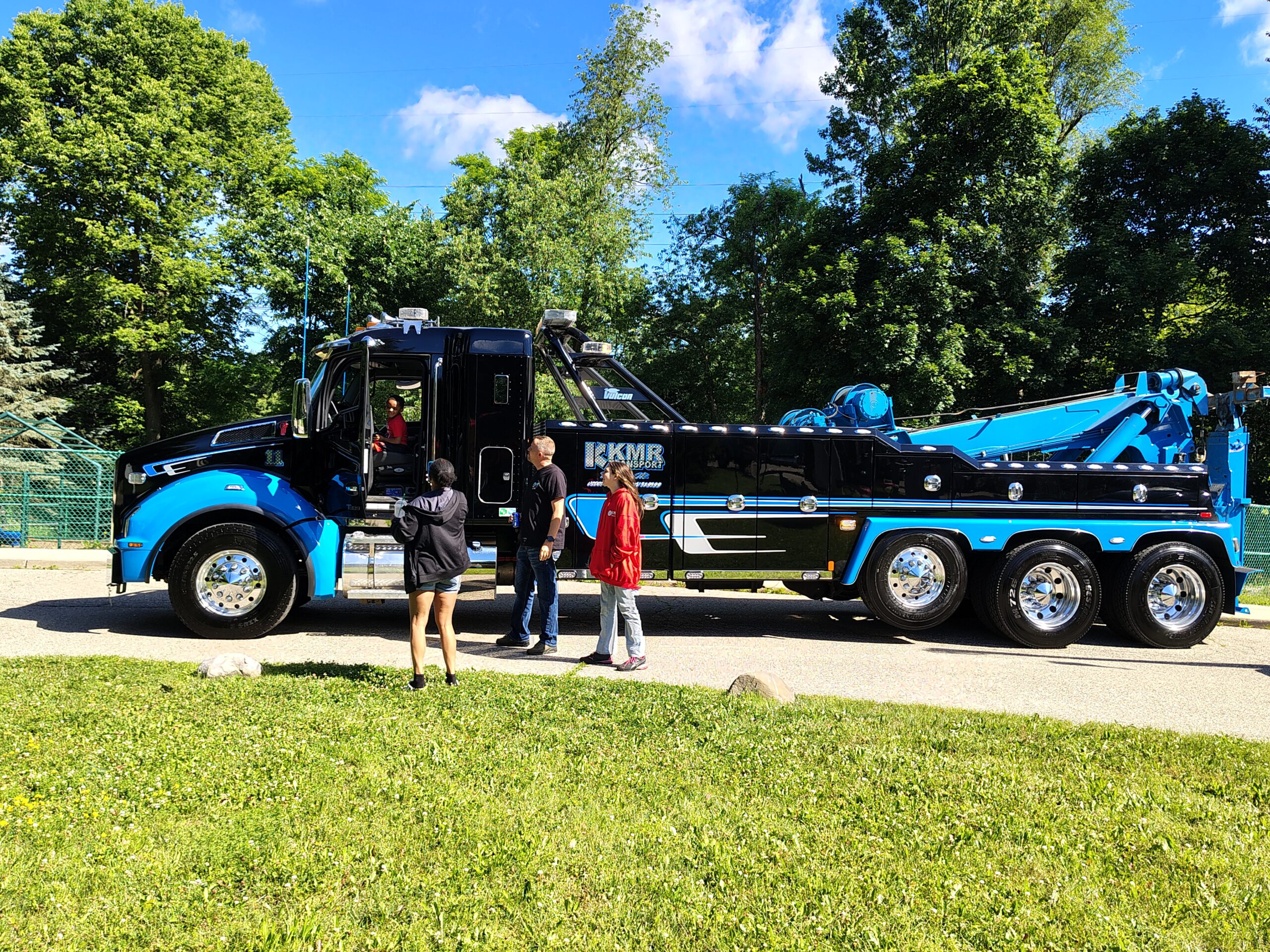 Kid enjoying sitting in the drivers seat of a large black and blue transportation truck.